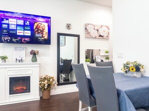 A hotel room with a flat-screen TV displaying a streaming service interface, a fireplace, a mirror, and a dining area with chairs and a table. - The Disney Oasis - Your Disney Day! - Your Spa Night! (Kissimmee)