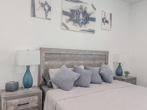A bedroom with a wooden headboard, a bed with grey bedding, two bedside tables with lamps, and abstract artwork on the wall. - The Disney Oasis - Your Disney Day! - Your Spa Night! (Kissimmee)