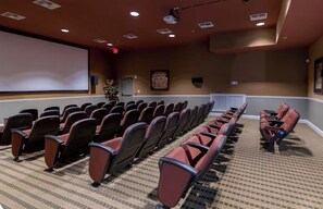 Un salón de conferencias con filas de sillas, una pantalla de proyector y suelo alfombrado.