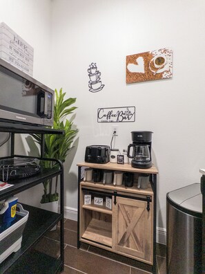 Una kitchenette equipada con microondas, tostadora, cafetera y estantes con tazas.