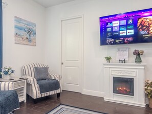 Una sala de estar con una televisión de pantalla plana montada en la pared, un sillón a rayas, una chimenea y un cuadro en la pared.