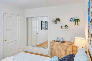 Ein Schlafzimmer mit einem Bett, einem Schminktisch, einem Spiegel, einer Tür und einer Wand mit Regalen.