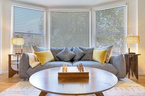 Een zithoek met een grijze bank, decoratieve kussens, een ronde salontafel en twee lampen.