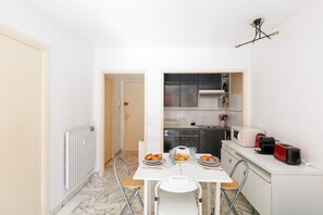 A compact kitchen with a dining table, chairs, and basic appliances. - Upstays Cosy T2 32m² with balcony and AC (Cannes)