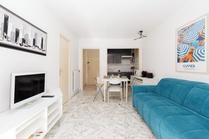 A modern living room with a blue sofa, a television, and a dining area with a table and chairs. - Upstays Cosy T2 32m² with balcony and AC (Cannes)
