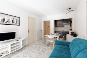 A compact living space with a TV, dining area, kitchenette, and a blue sofa. - Upstays Cosy T2 32m² with balcony and AC (Cannes)