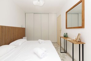 A hotel room with a bed, a wooden headboard, a bedside table with a mirror, and a wardrobe. - Upstays Cosy T2 32m² with balcony and AC (Cannes)
