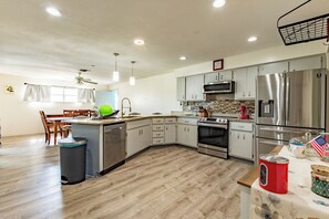 A modern kitchen with stainless steel appliances, wooden flooring, and a dining area with a table and chairs. - 4-Bedroom Lehigh Acres Getaway with Private Pool & Spa (Lehigh Acres)