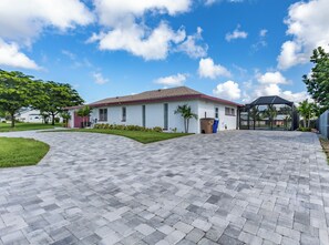 A residential house with a paved driveway, a covered outdoor area, and a well-maintained lawn. - 4-Bedroom Lehigh Acres Getaway with Private Pool & Spa (Lehigh Acres)