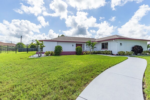 A single-story house with a red roof, a front yard with a curved driveway, and a clear sky. - 4-Bedroom Lehigh Acres Getaway with Private Pool & Spa (Lehigh Acres)