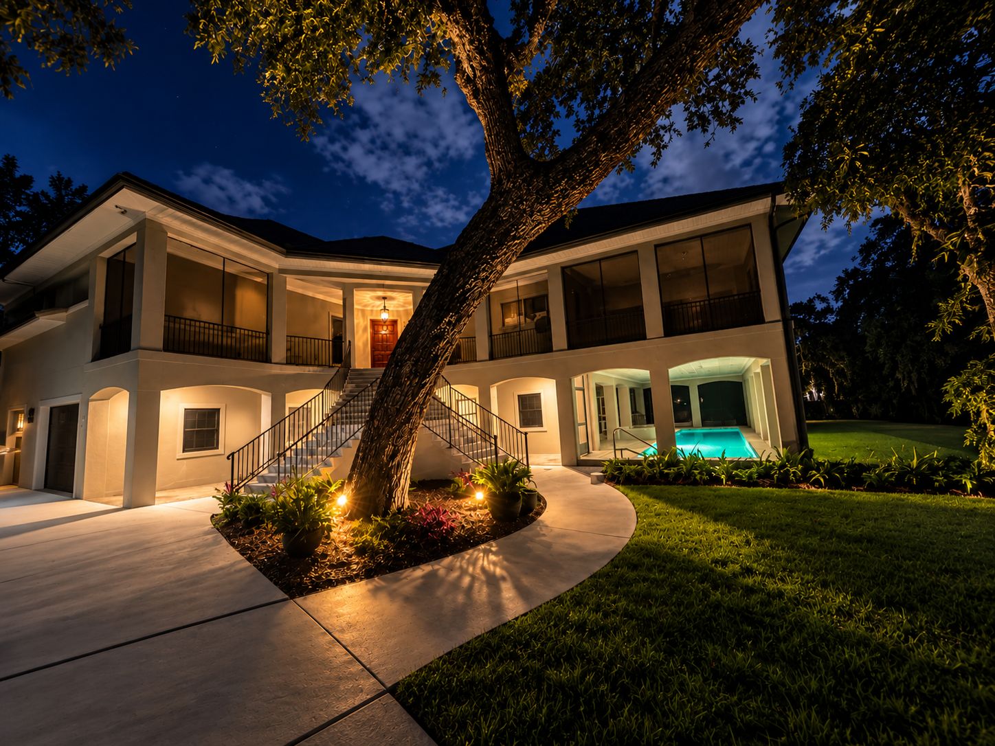A two-story house with a swimming pool, a large tree in the front yard, and a well-lit exterior.