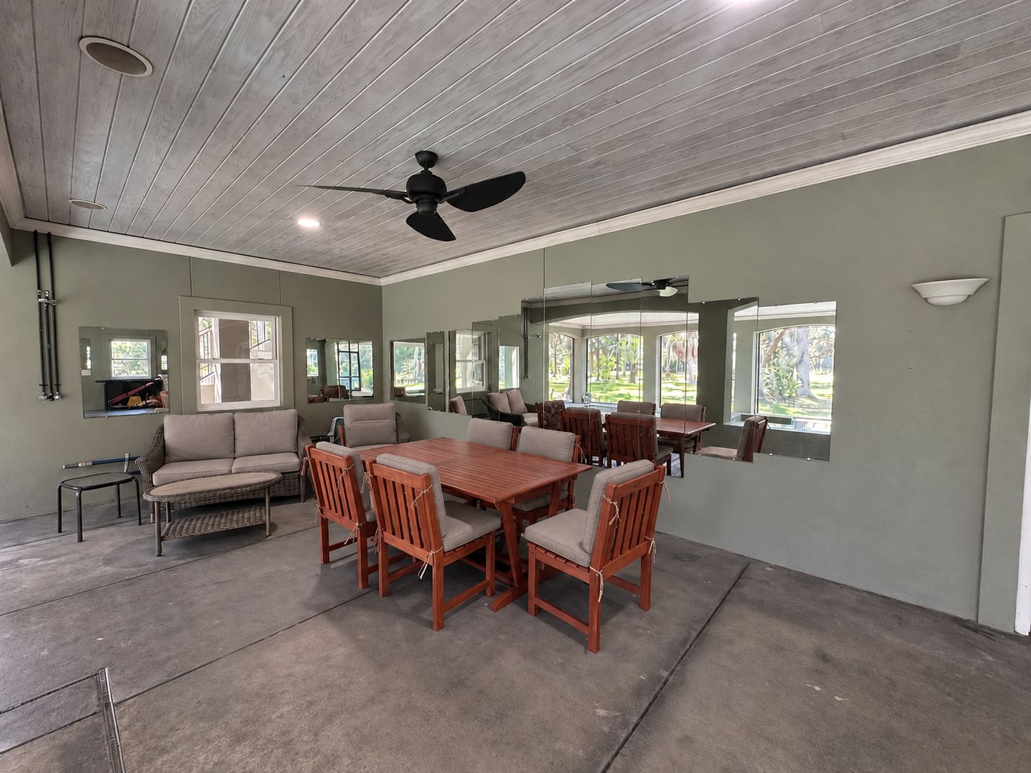 A dining area with a wooden table and chairs, a ceiling fan, and large windows.