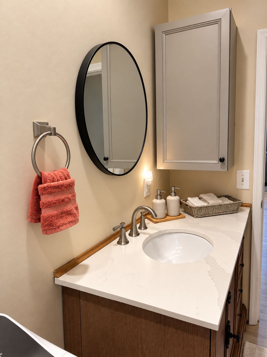 A bathroom with a white sink, a round mirror, a towel rack with a red towel, and a cabinet above the sink.