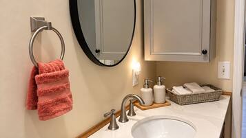 A bathroom with a white sink, a round mirror, a towel rack with a red towel, and a cabinet above the sink.