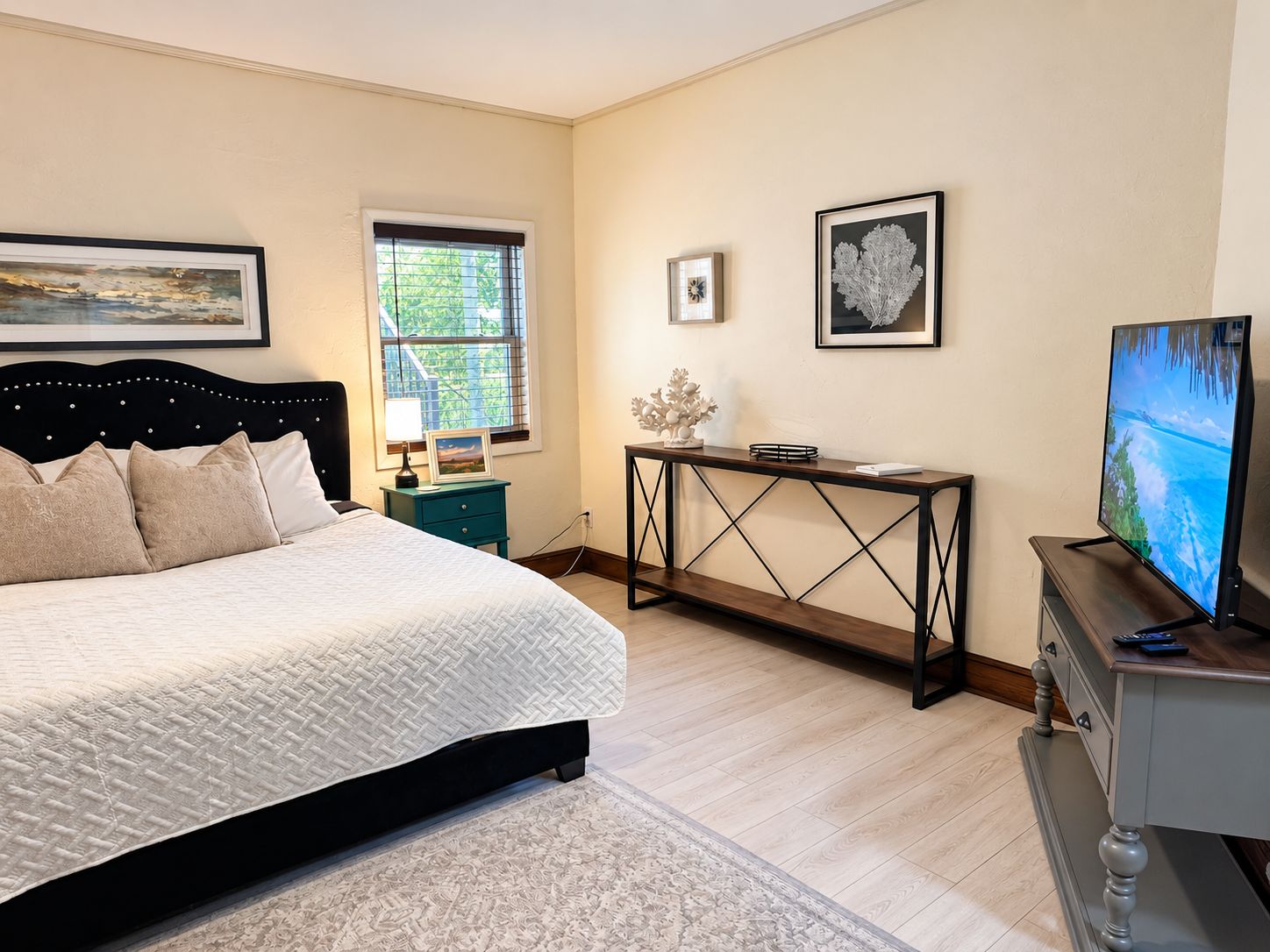 A bedroom with a bed, a desk, a television, and artwork on the walls.