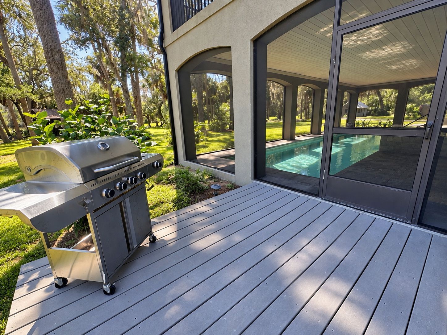 An outdoor deck with a grill and a swimming pool in the background.