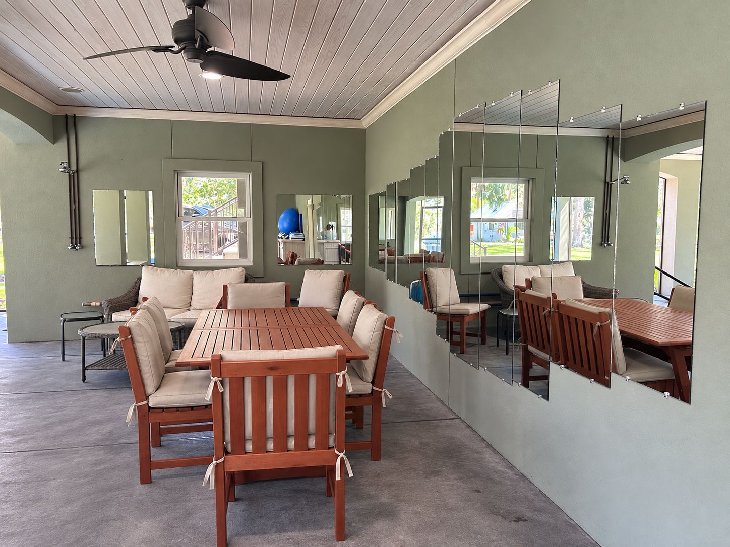 A room with a ceiling fan, a dining table with chairs, a sofa, and a large mirror on the wall.