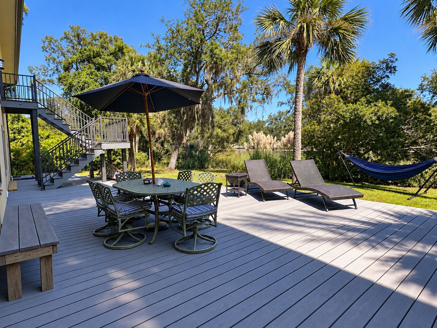 Une terrasse avec une table et des chaises, un hamac et un escalier menant à un niveau supérieur.