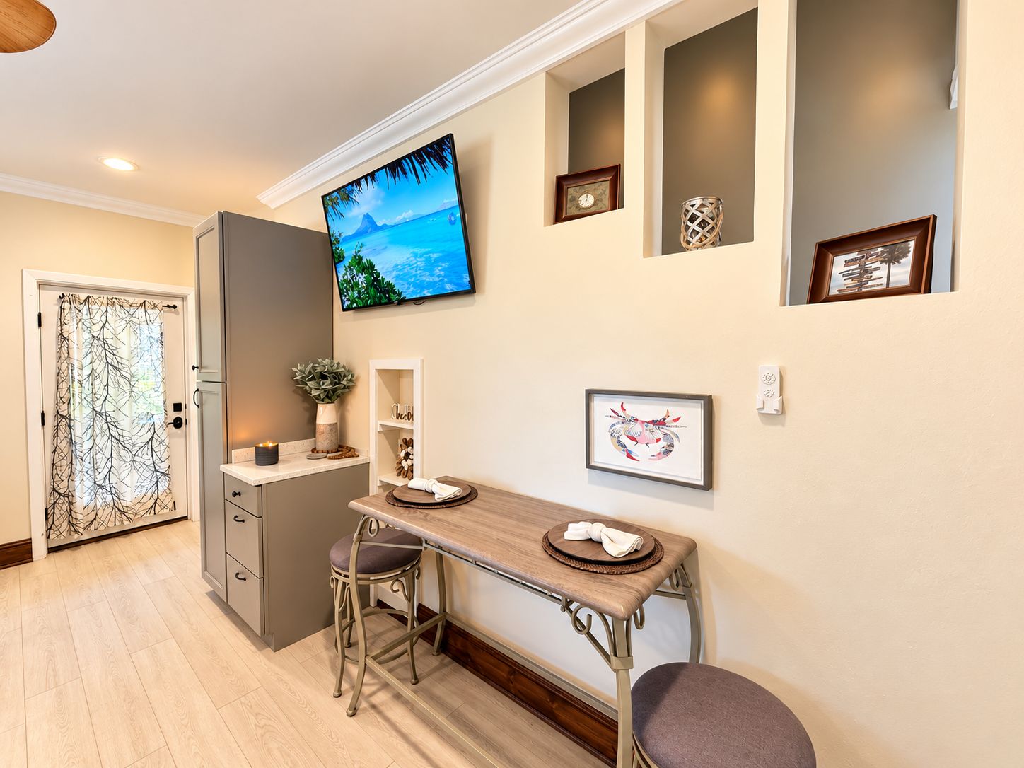A modern kitchen with a built-in oven, a dining area with a wooden table and bar stools, and a TV mounted on the wall.