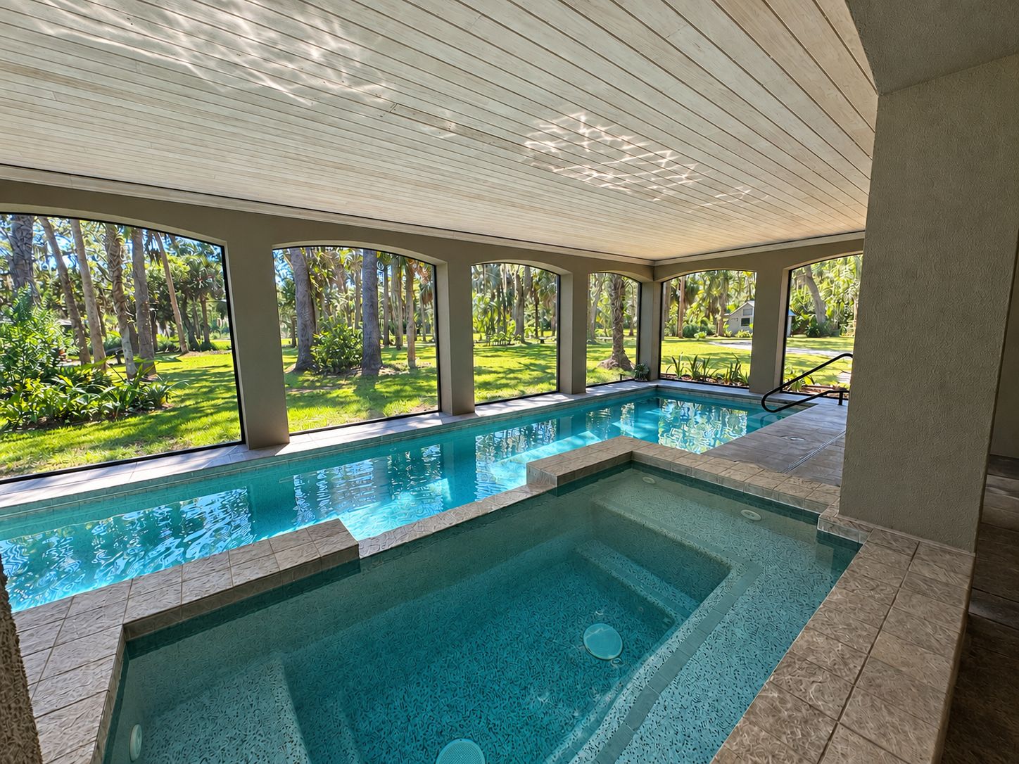 A swimming pool with a view of a tropical landscape, surrounded by a covered area with columns.