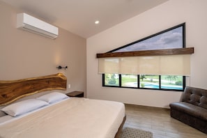A bedroom with a large bed, a wooden headboard, a nightstand, a chair, a window with a view of a swimming pool, and an air conditioning unit. - Brisas de Tamarindo | Pool in Front (Tamarindo)