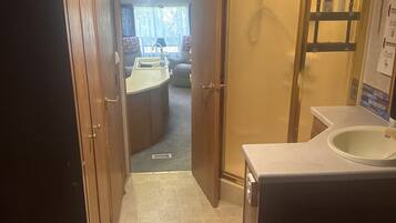 A compact RV interior with a kitchenette, a bathroom with a shower, and a seating area.