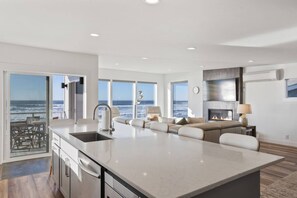 A modern kitchen with a large island, a dining area with a view of the ocean, and a living area with a fireplace. - Unforgettable Ocean Views From Home and Hot Tub, Fire Pit, Chef's Gourmet Kitchen, Steps From Beach (Rockaway Beach)