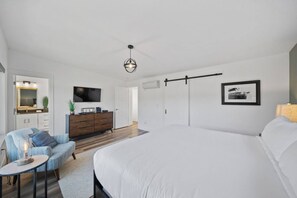 Een slaapkamer met een groot bed, een televisie, een dressoir en een deur naar een andere kamer.