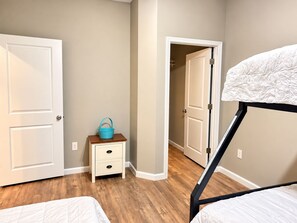 Un dormitorio con una cama individual superpuesta, una mesita de noche con una cesta azul y una puerta que da a otra habitación.