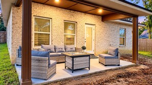 Un patio techado con mobiliario de mimbre, una chimenea y fachada de ladrillo.