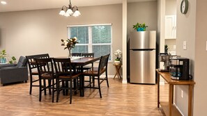 Une cuisine moderne équipée d’un réfrigérateur en acier inoxydable, d’une machine à café et d’un coin repas avec des chaises et une table en bois.