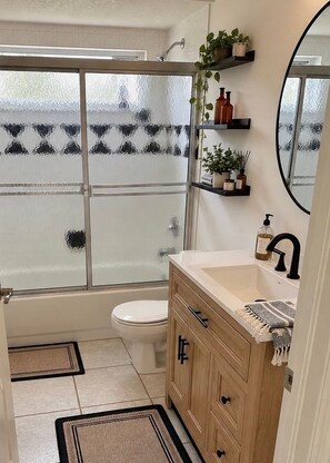Ein Badezimmer mit Duschkabine aus Glas, Toilette, Waschbecken mit Spiegel und Holzschränken.