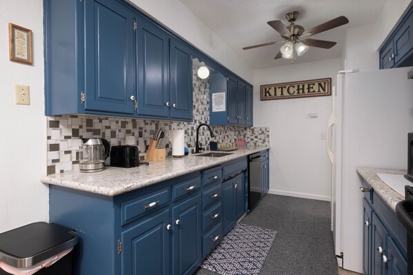 A kitchen with blue cabinets, a white countertop, a ceiling fan, and a 'KITCHEN' sign on the wall. - The Crew House! Spacious 4-bedroom & 3-Bathrooms with 7 Beds! (Amarillo)