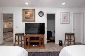 A hotel room with a television, two wooden stools, a framed picture, a clock, and a door leading to another room. - The Crew House! Spacious 4-bedroom & 3-Bathrooms with 7 Beds! (Amarillo)