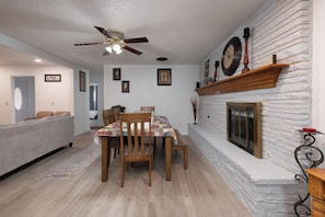 A dining area with a wooden table and chairs, a ceiling fan, and a fireplace with a stone wall. - The Crew House! Spacious 4-bedroom & 3-Bathrooms with 7 Beds! (Amarillo)