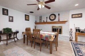 A dining area with a wooden table, chairs, a ceiling fan, and a brick wall with a clock. - The Crew House! Spacious 4-bedroom & 3-Bathrooms with 7 Beds! (Amarillo)