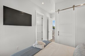 A bedroom with a bed, a flat-screen TV mounted on the wall, and two doors leading to other rooms. - 🌊 Palmilla at LBJ | Canal Front Pool, Boat Dock & Hill Country Lake Life 🚤 (Kingsland)