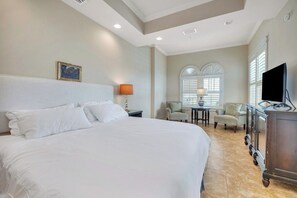 A hotel room with a large bed, a television, a desk with a lamp, and a window with blinds. - One bedroom with great ocean views! (St. Simons Island)