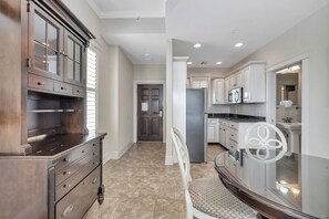 A spacious kitchen with modern appliances, a dining area with a glass table, and a hallway leading to a door. - One bedroom with great ocean views! (St. Simons Island)