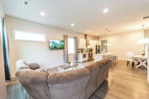 A modern living room with a sofa, a TV, and a dining area with chairs and a table. - Charming 4-bedroom house in Charlotte close to Uptown (Charlotte)