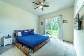 A bedroom with a large bed, a ceiling fan, a nightstand, a TV, and a sliding glass door leading to a balcony. - Charming 4-bedroom house in Charlotte close to Uptown (Charlotte)