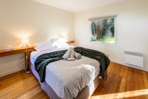 A bedroom with a bed, bedside lamps, a window with a view of greenery, and a wooden floor. - Proms Edge - Coastal Banksia Villa (Yanakie)