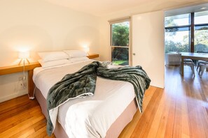 Un dormitorio con cama, mesita de noche, lámpara y vistas al exterior a través de una puerta.