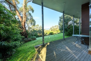 Uma área externa coberta com deck de madeira, uma mesa e cadeiras.