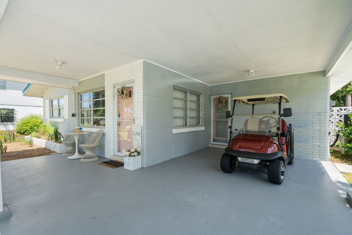 A covered patio area with a golf cart, outdoor seating, and a small table.