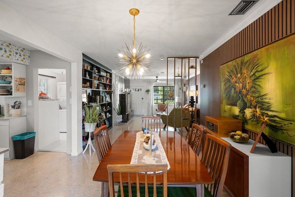 A modern dining area with a wooden table, chairs, and a unique ceiling light fixture. - Charming 2BR Retro Pondside Retreat FREE golf cart (New Port Richey)