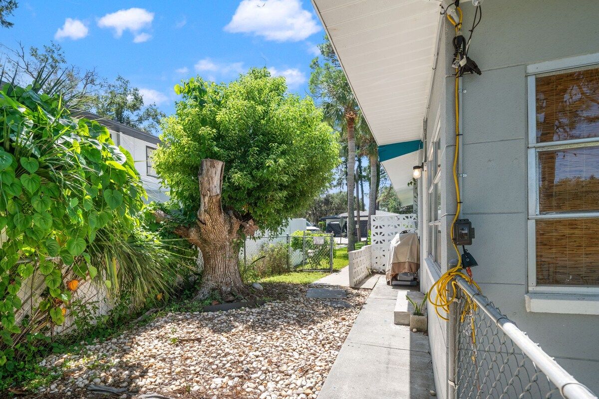 A residential property with a covered porch, a large tree, and a gravel pathway.