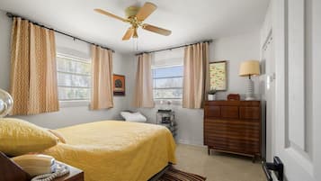 Un dormitorio con cama, cómoda, mesita de noche, lámpara y ventilador de techo.