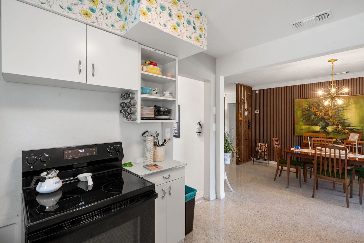 Une cuisine moderne avec des meubles blancs, une cuisinière noire et un coin repas comprenant des chaises et une table en bois.