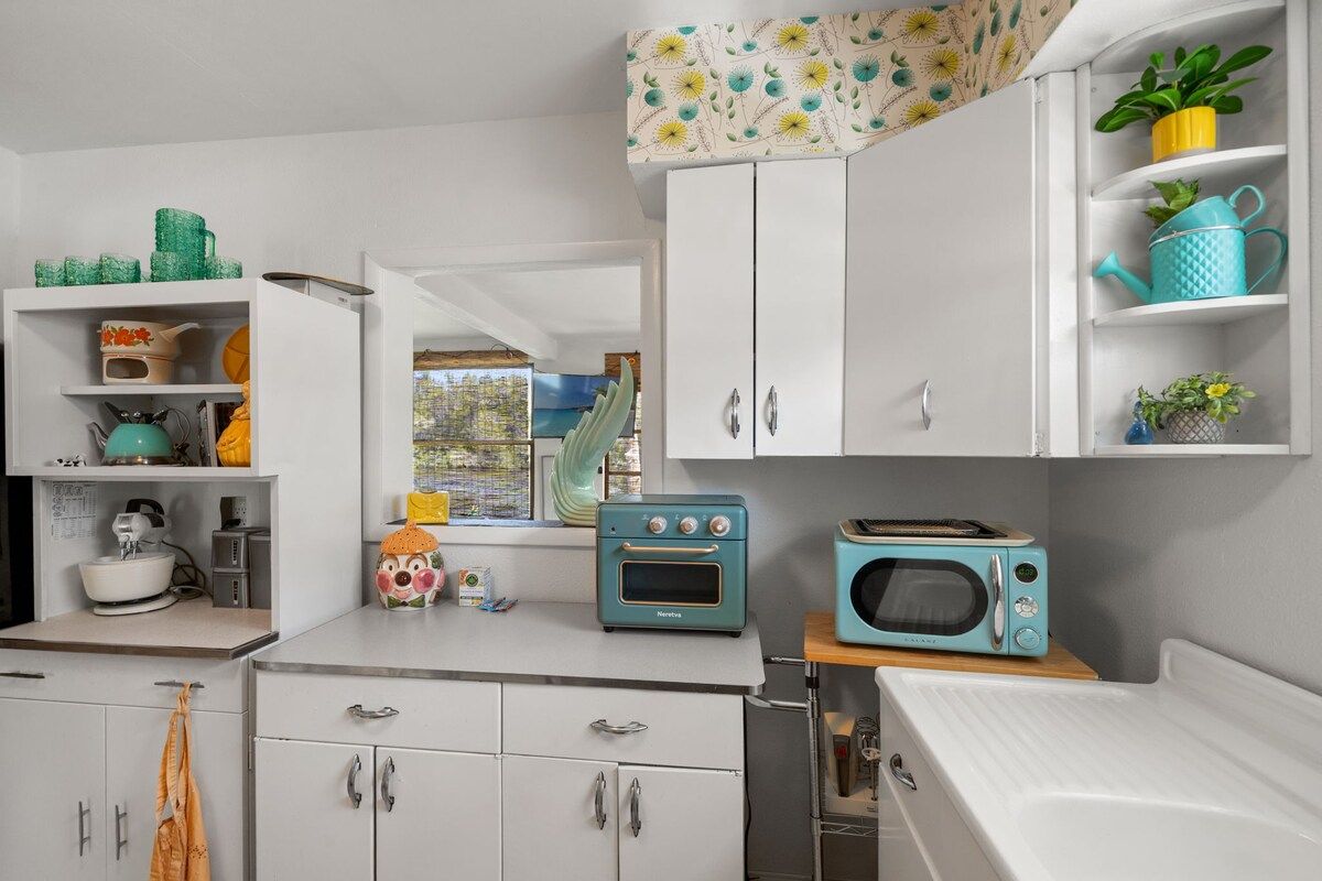 A kitchen with white cabinets, a microwave, a toaster, and a window with a view of greenery.